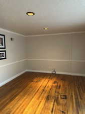 Empty room featuring hardwood / wood-style flooring, a textured ceiling, and ornamental molding
