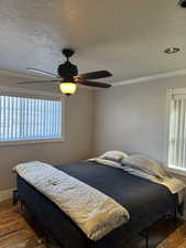 Bedroom featuring a textured ceiling, ceiling fan, wood-type flooring, and ornamental molding
