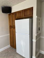 Kitchen with wood finish cabinetry, freestanding refrigerator, a textured ceiling, and light tile patterned floors