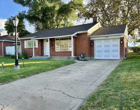 Single story home featuring concrete driveway, a shingled roof, an attached garage, brick siding, and a chimney