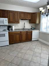 Kitchen with white appliances, a textured ceiling, a chandelier, light tile patterned floors, and wood finish cabinets