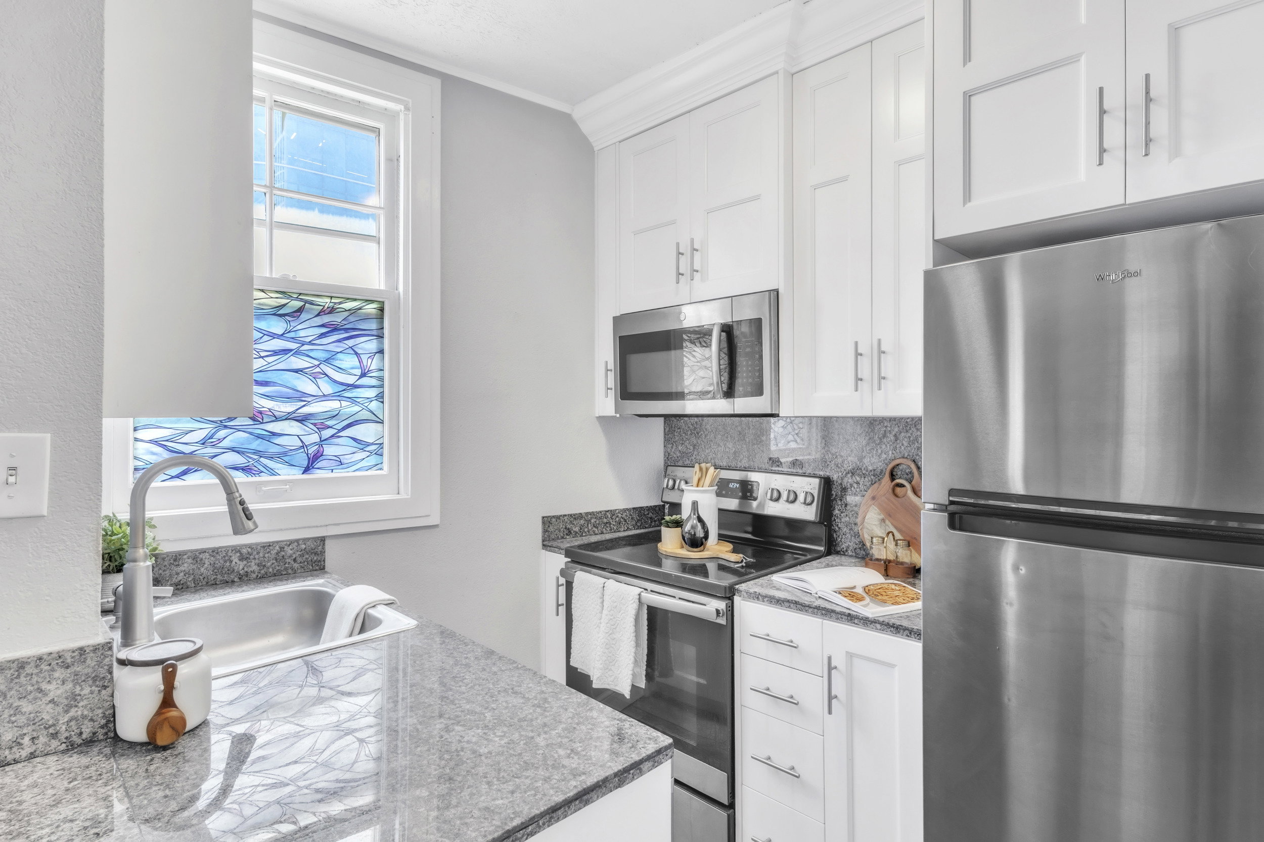 Kitchen with stainless steel appliances, white cabinetry, dark stone counters, backsplash, and crown molding