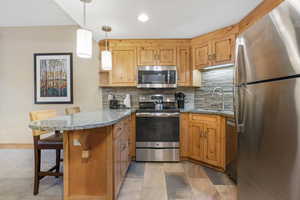 Kitchen featuring a peninsula, a breakfast bar area, stainless steel appliances, backsplash, and granite countertops