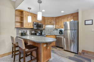 Kitchen with a peninsula, stainless steel appliances, open shelves, decorative light fixtures, and a breakfast bar area