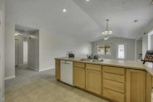 Kitchen with light wood finish cabinets, light countertops, dishwasher, lofted ceiling, and light colored carpet