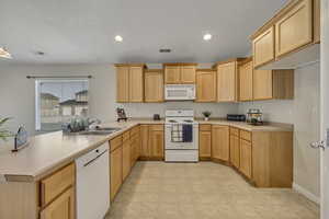Kitchen with a peninsula, white appliances, light countertops, light wood finish cabinets, and recessed lighting