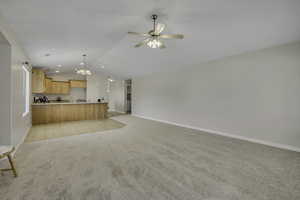 Unfurnished living room with suspended lighting, a ceiling fan, and light colored carpet