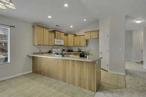 Kitchen with a peninsula, light countertops, light wood finish cabinetry, white appliances, and recessed lighting