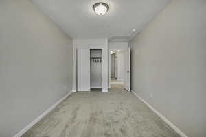 Unfurnished bedroom featuring a textured ceiling, light colored carpet, and a closet