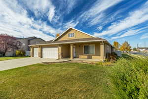 View of front facade featuring stucco siding, covered porch, a front yard, driveway, and an attached garage