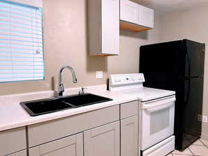Kitchen featuring white range with electric cooktop, white cabinetry, freestanding refrigerator, and light tile patterned floors