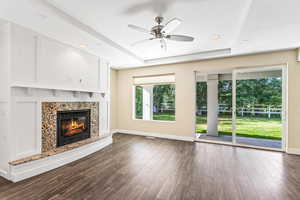 Unfurnished living room with a ceiling fan, dark wood-type flooring, a premium fireplace, a tray ceiling, and recessed lighting