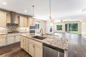 Kitchen with cream cabinets, stainless steel appliances, dark wood-type flooring, and light stone countertops