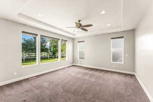 Carpeted spare room with a ceiling fan, plenty of natural light, recessed lighting, and a tray ceiling