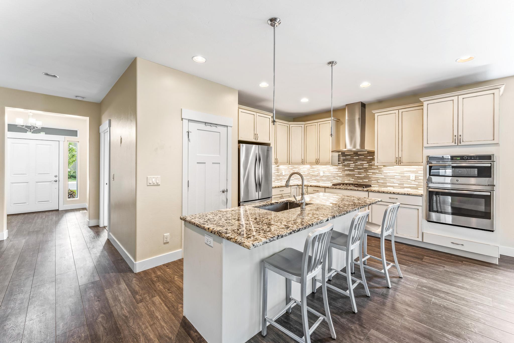 Kitchen with light stone countertops, stainless steel appliances, a kitchen breakfast bar, a kitchen island with sink, and dark wood-type flooring