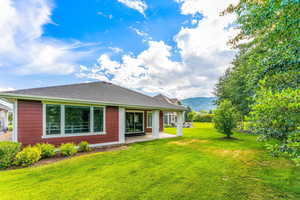 Back of house featuring a patio, a lawn, and roof with shingles