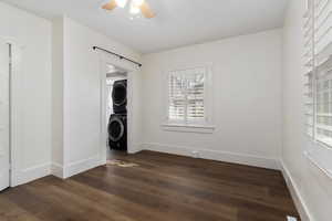 Spare room with stacked washing machine and dryer, dark wood finished floors, and a ceiling fan