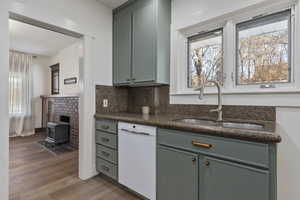 Kitchen featuring white dishwasher, a wood stove, backsplash, dark stone countertops, and light wood-type flooring