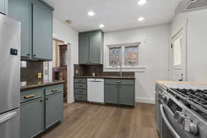 Kitchen featuring stainless steel appliances, light wood-type flooring, dark stone counters, recessed lighting, and green cabinets
