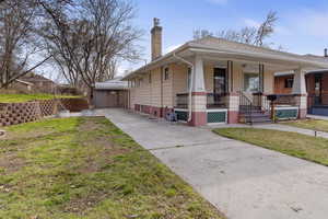 View of front facade featuring a front lawn, a chimney, a porch, driveway, and an outbuilding