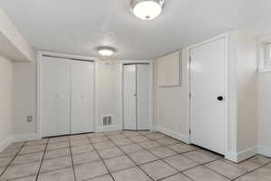 Unfurnished bedroom with two closets, a textured ceiling, and light tile patterned floors