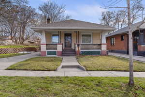Bungalow-style home featuring a chimney, covered porch, a shingled roof, and a front lawn