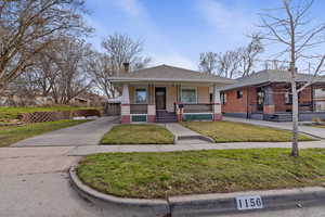 View of front of property featuring covered porch, a chimney, a shingled roof, and a front yard