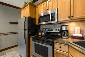 Kitchen with stainless steel appliances, dark stone counters, decorative backsplash, and light stone finish flooring