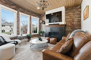 Living area featuring brick wall, wood ceiling, a glass covered fireplace, and hanging lights