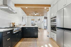 Kitchen with stainless steel appliances, a peninsula, range hood, light wood-type flooring, and ceiling fan