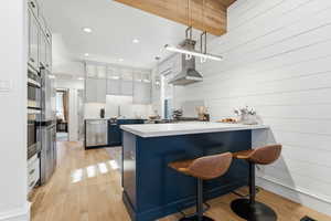 Kitchen featuring a peninsula, light wood-style flooring, a breakfast bar, blue cabinetry, and glass insert cabinets