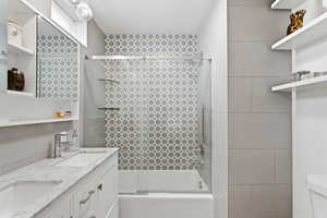 Full bathroom with combined bath / shower with glass door, double vanity, and tile walls