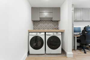 Laundry room with a desk, washer and dryer, cabinet space, and light wood-style flooring