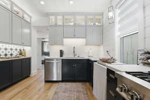 Kitchen with two tone cabinets, glass fronted cabinets, stainless steel appliances, light wood-style flooring, and light stone counters