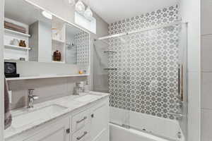 Full bath featuring tasteful backsplash, double vanity, and combined bath / shower with glass door