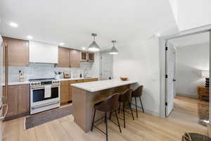 Kitchen with white range, a breakfast bar, extractor fan, light wood finished floors, and a peninsula