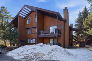 Snow covered back of property featuring a chimney and a balcony