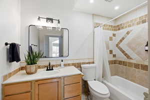 Bathroom with tile walls, vanity, wainscoting, shower / bathtub combination with curtain, and recessed lighting