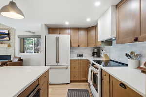 Kitchen with white appliances, wood finish cabinetry, light stone counters, light wood-type flooring, and pendant lighting
