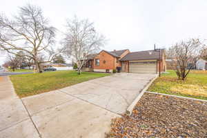 View of front facade featuring driveway, brick siding, a front lawn, a garage, and a chimney