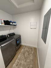 Laundry area with electric panel, light wood-style flooring, washer and dryer, and a tray ceiling