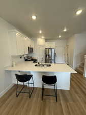 Kitchen with a kitchen breakfast bar, a peninsula, white cabinetry, stainless steel appliances, and light wood finished floors