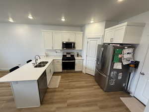 Kitchen with a peninsula, a breakfast bar, stainless steel appliances, light wood finished floors, and white cabinetry