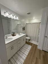 Bathroom with double vanity, dark wood-style floors, a textured ceiling, and shower / bath combo