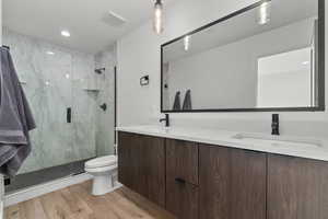 Full bath with double vanity, a marble finish shower, light wood-style flooring, and recessed lighting