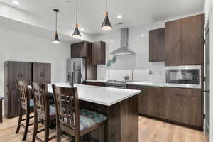 Kitchen featuring modern cabinets, ventilation hood, dark wood finish cabinets, a kitchen island with sink, and pendant lighting