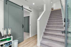 Staircase with a barn door, wood finished floors, and recessed lighting