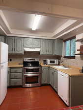 Kitchen featuring light countertops, a tray ceiling, white appliances, dark tile patterned flooring, and backsplash