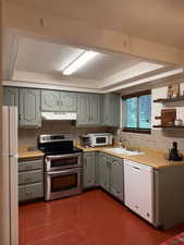 Kitchen featuring white appliances, dark tile patterned flooring, light countertops, backsplash, and a tray ceiling