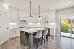 Kitchen with decorative light fixtures, a kitchen bar, light wood-style flooring, a center island, and stainless steel appliances